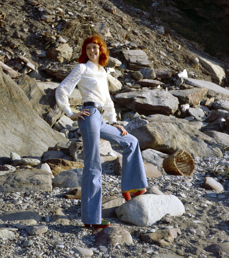 Tall natural redhead Erika on a North Devon beach in the UK, wearing bell bottom jeans.
